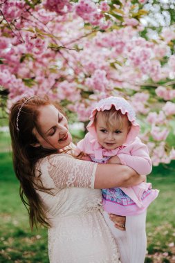 Anne ve bebek kız üzerinde arka plan çiçek pembe çiçekleri kiraz ağacının bahar sevgi dolu. Açık havada bahçe çiçekleri arasında kızı ile güzel bir kadın. Aile niteliğine Greenwich Park, İngiltere