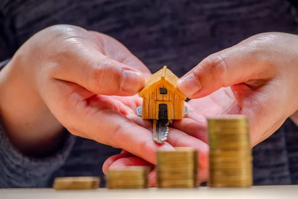 House or Home model and coins on hand with home key. Concept for loan, property ladder, financial, mortgage, real estate investment, taxes and bonus.