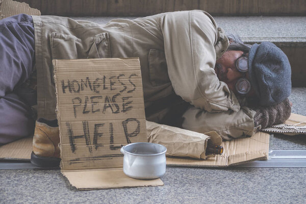 Businessman with suit donate some money in the metal bowl to help homeless man and he is sleeping on street or walkway in the city.