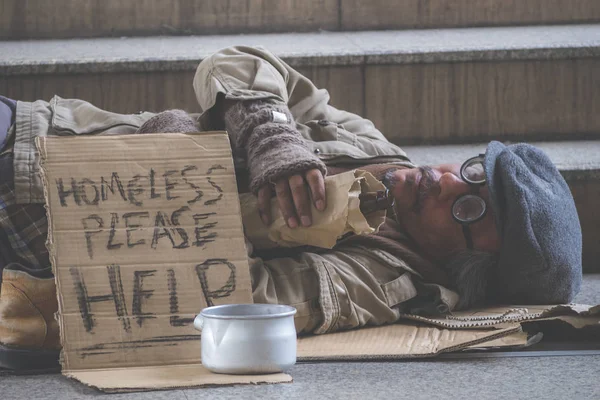スーツを着たビジネスマンは ホームレスの男性を助けるために金属ボウルにいくつかのお金を寄付し 彼は市内の通りや歩道で眠っています — ストック写真