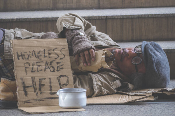 Businessman with suit donate some money in the metal bowl to help homeless man and he is sleeping on street or walkway in the city.