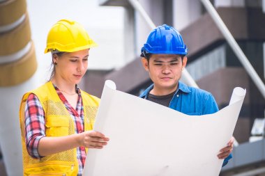 İnşaat işçileri ve mühendis ekibi koruyucu kask giyen ve proje detayları tartışmak ve planları ile yerinde duran, denetim için araçlar onları iş.
