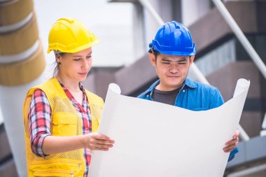 İnşaat işçileri ve mühendis ekibi koruyucu kask giyen ve proje detayları tartışmak ve planları ile yerinde duran, denetim için araçlar onları iş.
