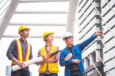 İnşaat işçileri ve mühendis ekibi koruyucu kask giyen ve proje detayları tartışmak ve planları ile yerinde duran, denetim için araçlar onları iş.