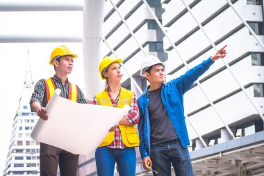 İnşaat işçileri ve mühendis ekibi koruyucu kask giyen ve proje detayları tartışmak ve planları ile yerinde duran, denetim için araçlar onları iş.