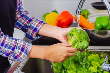 Genç kadın mutfakta pişirmeden önce pestisitleri kaldırmak için brokoli yıkıyor. Meyve ve sebze yıkama konsepti.