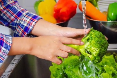 Genç kadın mutfakta pişirmeden önce pestisitleri kaldırmak için brokoli yıkıyor. Meyve ve sebze yıkama konsepti.