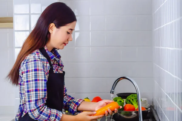 Young woman washing carrot to remove pesticides before cooking in kitchen. Fruit and vegetables washing concept.