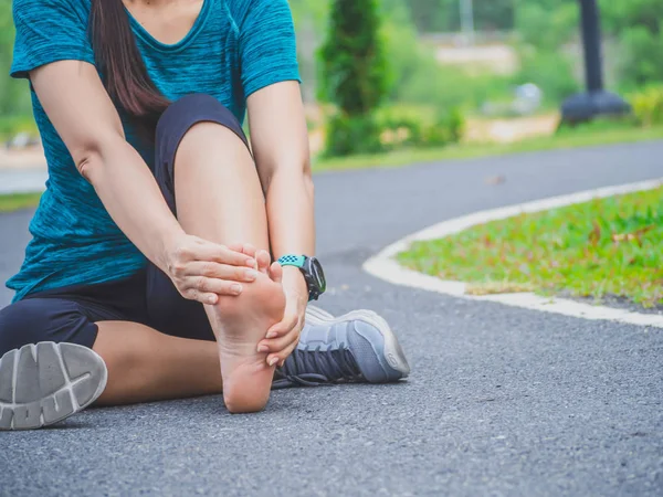 Sport woman suffering from pain in ankle while sitting on street in garden.