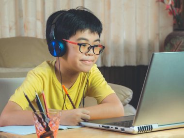 Kulaklık takan çocuk internette sohbet eden Skype öğretmeniyle masada oturuyor sınava hazırlanıyor ve ödevi için dizüstü bilgisayar kullanıyor ve online eğitim için E-öğrenim görüyor. çocuk konsepti öğrenmek.