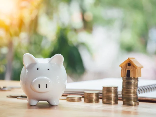 Model house placed on gold stack coins and piggy bank in front of the notebook.To save money invest for future. Concept for loan, property ladder, financial, real estate investment, taxes and bonus.