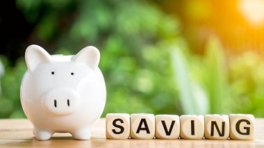 Tahta bloğa yakın beyaz domuz kumbarası ya da gelecek için ahşap bir masada tasarruf sözcüğünün küpü. Konsept kredi, emlak merdiveni, mali, gayrimenkul yatırımı ve ikramiye.