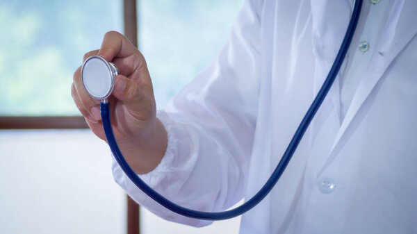 Male medicine doctor hand holding stethoscope against of chest on hospital background. Physician ready to examine patient. Medical and patient care concept.