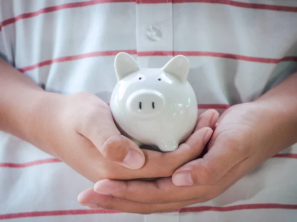 Portrait of teen boy holding and giving white piggy bank in garden. Concept for saving money, loan, property ladder, financial, real estate investment and bonus.