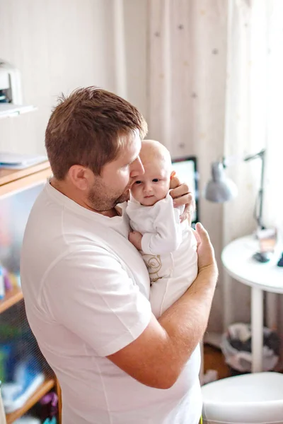 Um pai gentilmente segura sua filha de três meses em seus braços em um quarto desordenado — Fotografia de Stock