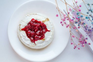 Derginin arka planında çilek sosuyla pişirilmiş peynirli camembert peyniri. Çiçek dalı ile süslenmiş. Parlak floresan ışığı. Yukarıdan görünüşü