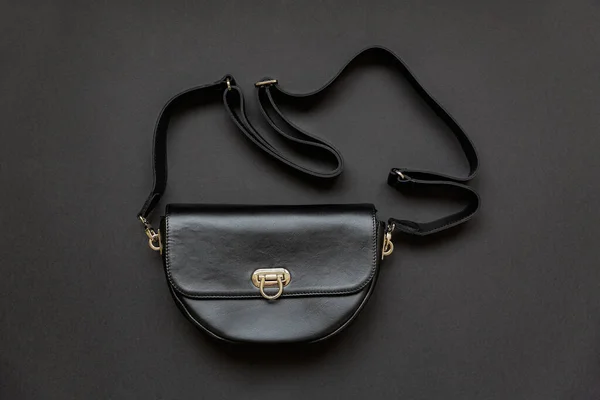 Black leather womens messenger bag with a belt on a black background