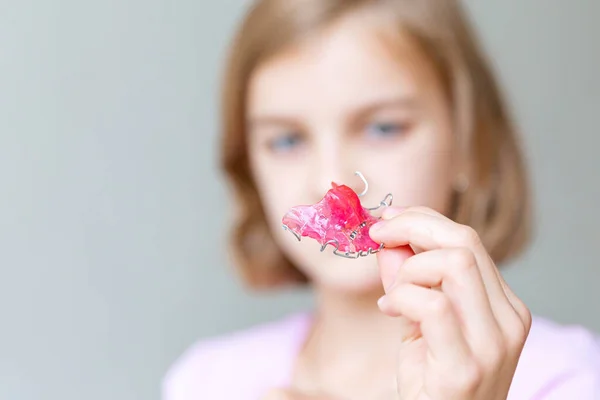 A menina segura uma placa ortodôntica rosa em suas mãos e mostra. — Fotografia de Stock