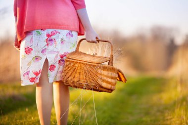 Genç bir kadın tarlaya doğru yürüyor ve elinde çimlerle hasır bir sepet taşıyor..