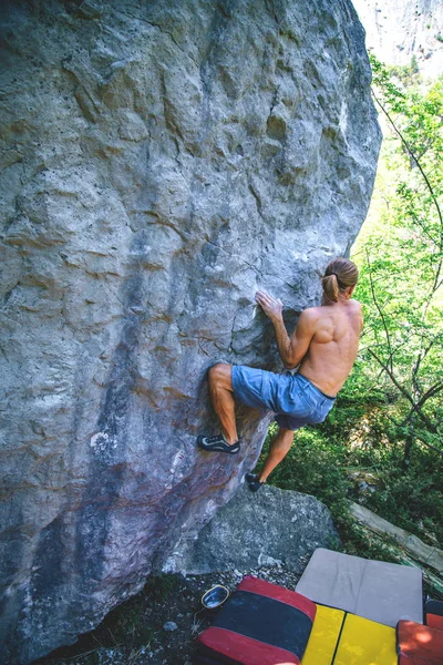 Athletic man climbing hard boulder problem in forest using special crash pads. Sport climbing, bouldering. Outdoor.