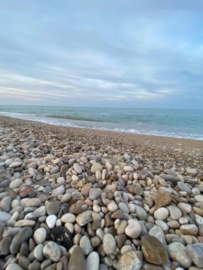 Pineto, İtalya, Adriyatik suları yakınlarındaki yorgan çakıl taşları bulutlu gökyüzü altında kayalık kıyı arazisini hafifçe kaplıyor