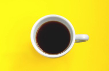 Sarı arka planda izole edilmiş beyaz bir fincanda sade kahve. Seçici odaklanma. Üst görünüm