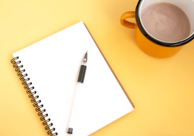 Kalemle birlikte beyaz bir defter aç ve narin bir arka planda kakaolu demir turuncu bardak. Düz yatıyordu. Seçici odak