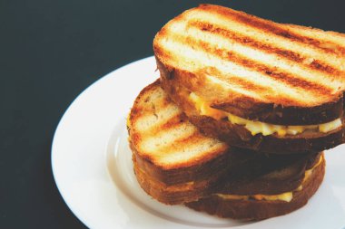 Izgara tost sandviçi, beyaz tabakta, siyah bir arka planda.