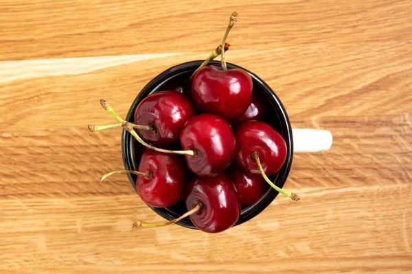 Red ripe cherries in a white iron mug in the center of a wooden background. Close-up of cherries. Background with copy space