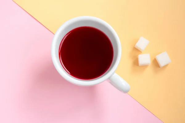 Red hibiscus tea in a white cup with pieces of sugar on orange and pink background — Stock Photo, Image