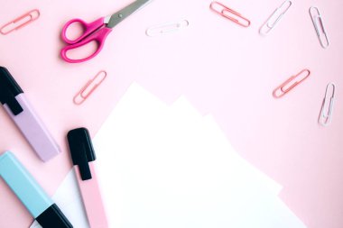 Beyaz not defteri, pembe, mavi ve yeşil kalemler, ataç, makas, pembe arka planda silgiler, yazı için boşluk. Okul kırtasiyesi. Okula, yaratıcı çalışma alanına. Renkli kırtasiye seti