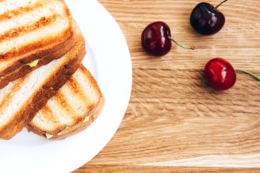 Beyaz tabakta yumurta ve kırmızı kirazlı ızgara tost sandviç.