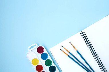 Okula geri döndüm, suluboya, fırça ve mavi arka planda not defteriyle yatıyordum.