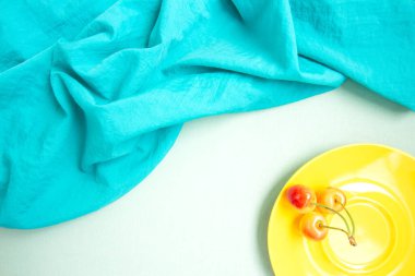 Turkuaz kumaş ve sarı kirazlı sarı tabak. Taze meyve.