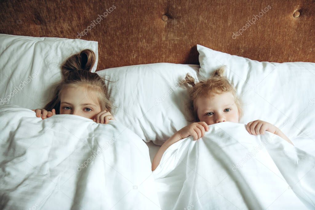 Two children hiding under duvet in bed
