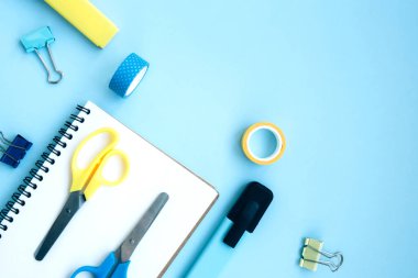 İşaretli, kıskaçlı, makasla, klipsli ve mavi arkaplanlı beyaz defter ve metin için boşluk. Okula hazırlanıyorum. Kırtasiyeli yaratıcı çalışma alanı. Okula dönelim. Düz yatıyordu