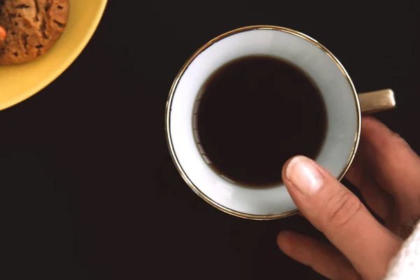 Женская рука держит золотой фарфоровой чашки кофе на черном фоне. — стоковое фото