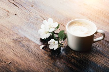 Bir fincan kahve ve tahta bir masada çiçek açan elma ağacı.