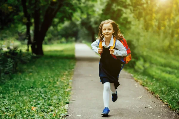 A girl in a school uniform and a backpack runs along the road to the park, the concept of the beginning of the school year