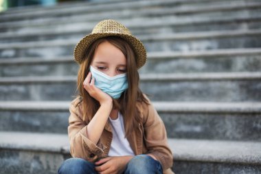 Tıbbi maskeli bir çocuk merdivenlerde oturur. Tecrit edilmiş çocuklar için yeni bir gerçeklik