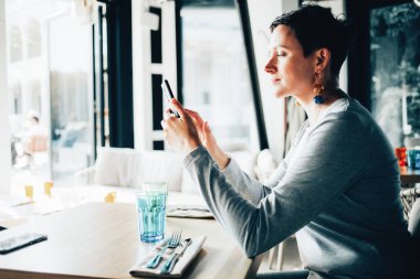 Caddedeki kafede telefonundan mesaj okuyan bir kadın.