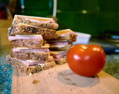 Kesme tahtasıüzerinde peynir ve jambon ile Sandviç, bulanık mutfak arka planda bulanık domates. Yakın çekim