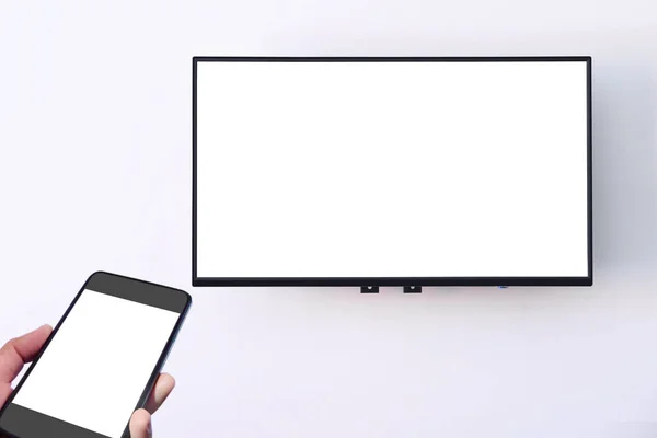手持白色智能手机屏幕和白色宽屏智能电视数字挂在白色墙壁背景 智能技术概念和复制空间和输入文本的想法 — 图库照片