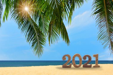 Yeni yıl 2021. Hindistan cevizi palmiye yapraklarıyla tropikal plajda bulutlu bir arka plan, mutlu bayram konsepti ve doğal rahatlama fikri.