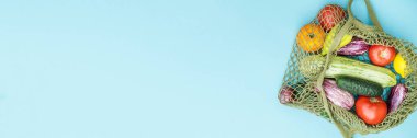 Mavi arka planda çeşitli taze sebzelerle yeşil iplik torbası. Sıfır atık kavramı, yeniden kullanılabilir ağ torbalarında taze sebzeler. Pankart.