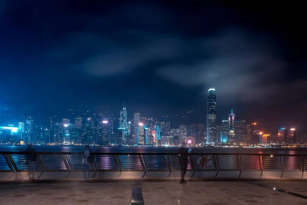 Hong Kong cityscape at night. Tourists walking on the waterfront