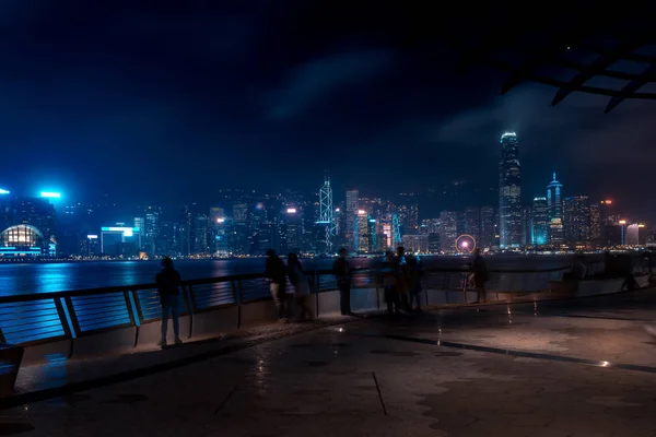 夜の香港の街並み。ウォーター フロントの上を歩く観光客 — ストック写真