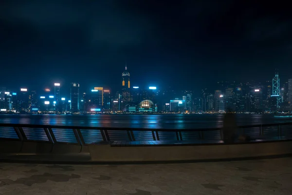 Paisaje urbano de Hong Kong por la noche. Turistas caminando por el paseo marítimo —  Fotos de Stock