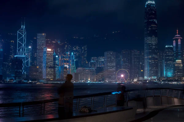 Paisaje urbano de Hong Kong por la noche. Turistas caminando por el paseo marítimo —  Fotos de Stock