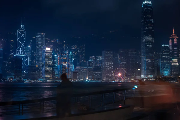 Paisaje urbano de Hong Kong por la noche. Turistas caminando por el paseo marítimo —  Fotos de Stock